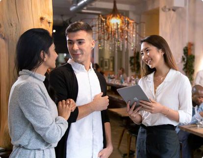 Restaurant worker holding a tablet while talking to customers ready to be seated