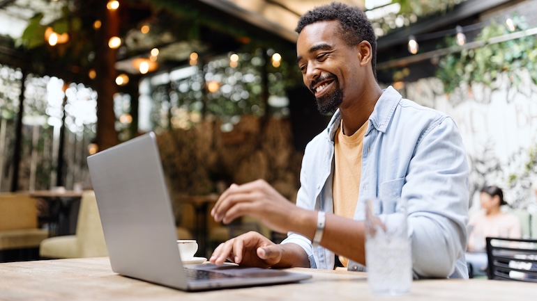Man sitting at a table at a restaurant with his laptop and a glass of water.
