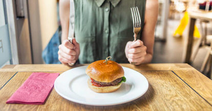 Diner holding up a fork and knife with a plate of food in front of her