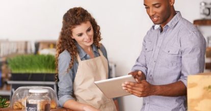 A man holding an iPad pointing at the screen talking to a woman who is also looking at the screen.