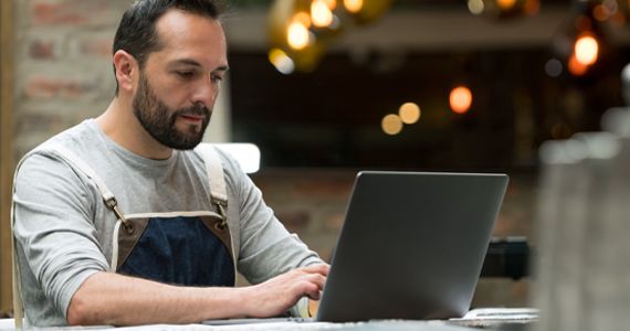 Restaurant employee typing on his laptop at a table