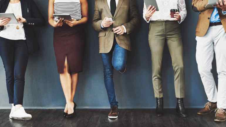 Row of people standing against a wall wearing different kinds of shoes