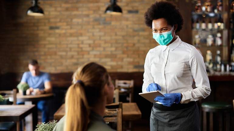 Server in mask and gloves taking order from patron