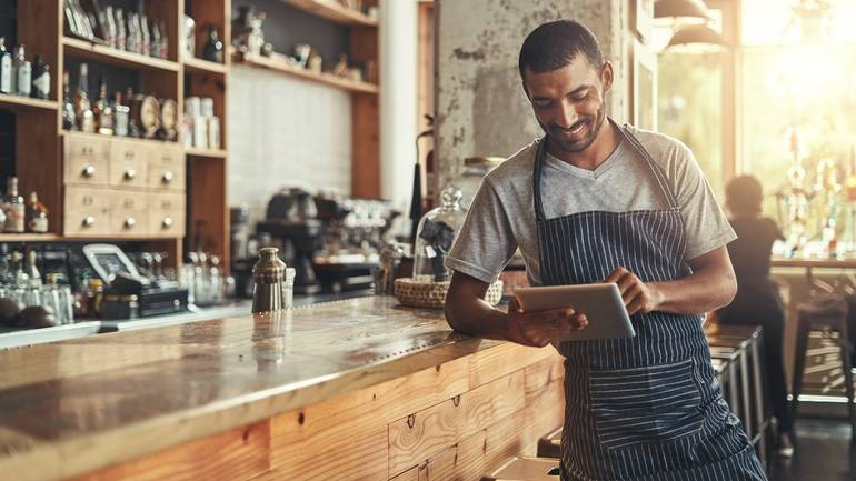 A cafe owner using an iPad while standing at the counter.