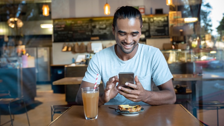 Young man using a phone to access a rewards program in a restaurant.