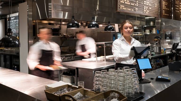 server using POS in busy restaurant kitchen