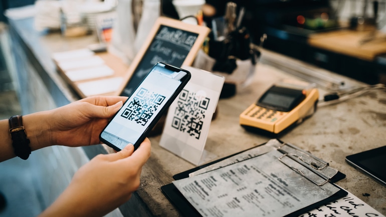 Customer scanning QR code in a cafe to make a quick and easy contactless payment with her smartphone.