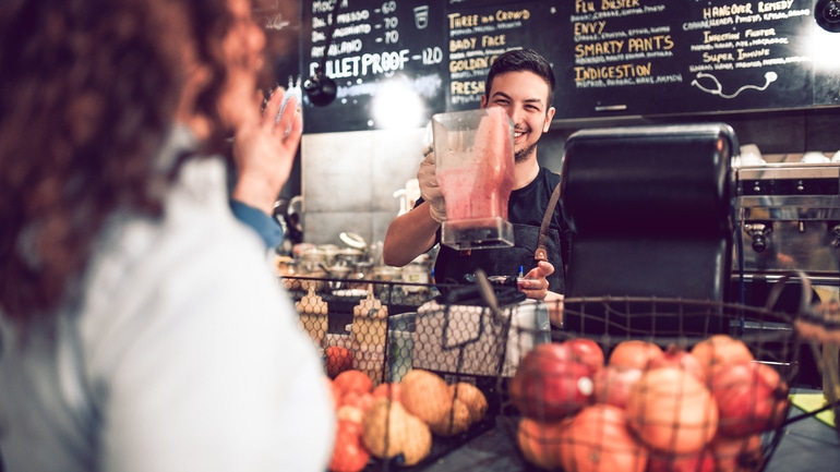 Smiling smoothie shop worker preparing a drink for a customer.