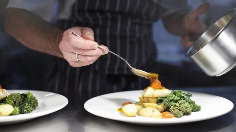 Chef preparing and plating a dish in restaurant kitchen.