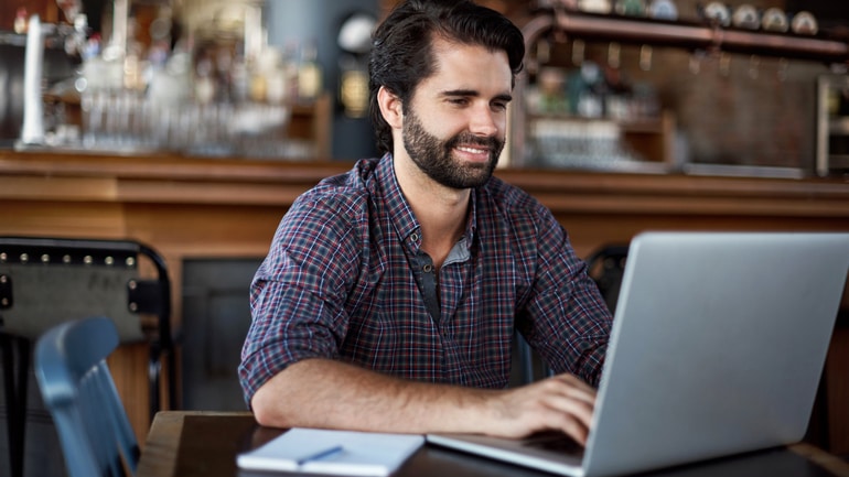 Man reads a newsletter on his laptop in a restaurant.