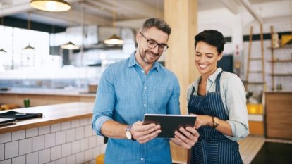 A man and woman at a restaurant smile and look together at a tablet device.