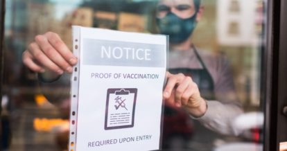 Restaurant worker wearing a face mask posting a sign in the window that says 