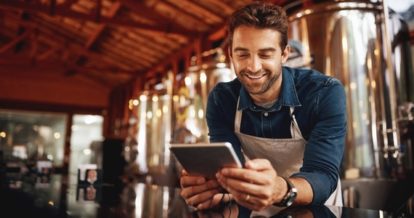 A smiling man using a tablet in a brewery.