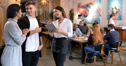 woman greets guests at a restaurant while holding a teblet.