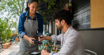 Latin American man making a contacless payment to the waitress at a restaurant using his cell phone