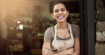 Smiling woman standing outside of a restaurant in the sun.