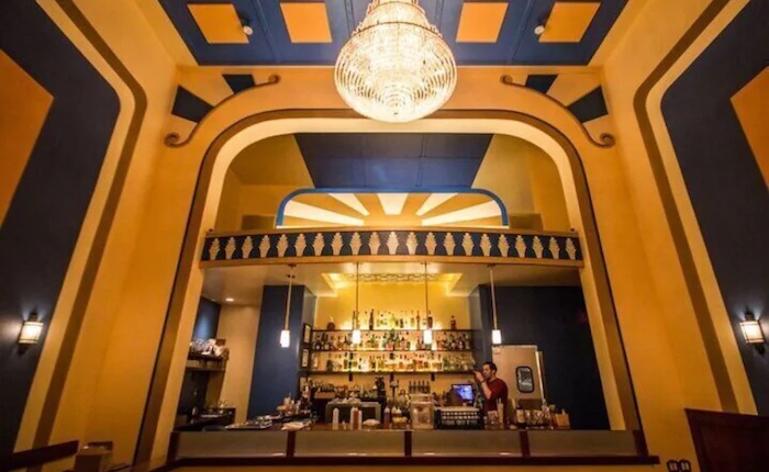 A bright yellow and royal blue bar with a dramatic chandelier hanging overhead.