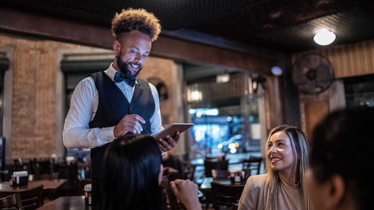 Server using a tablet to take guests' orders at a restaurant.