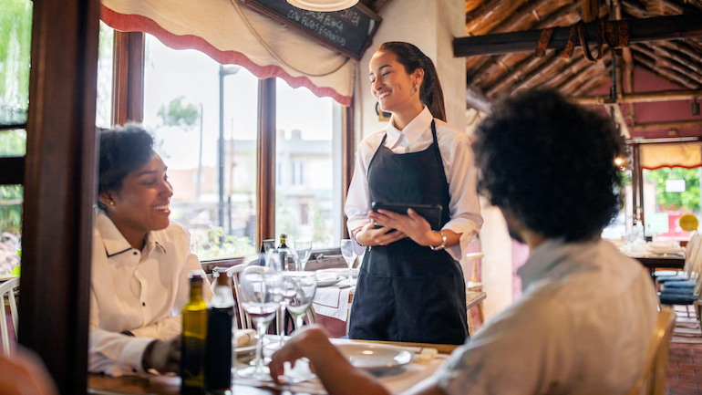 Sever talking to two guests at a table.