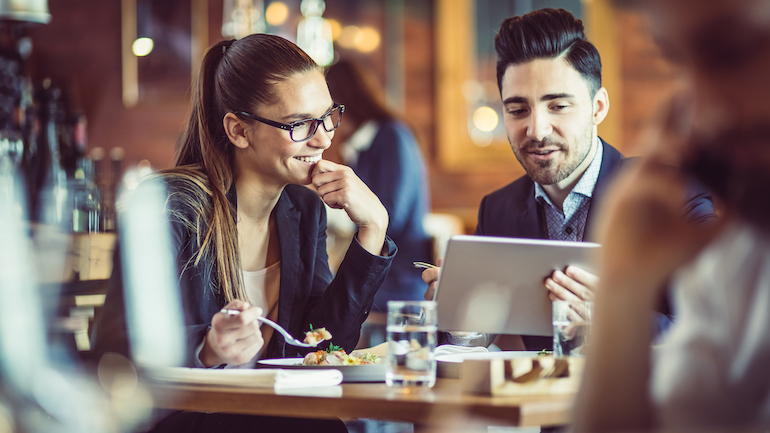 Two people eating at a restaurant while having a business meeting.