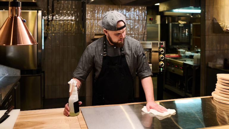 Chef working at a restaurant standing in front of a stove and cleaning the surface of it.