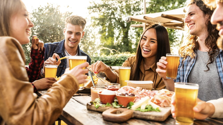 Happy group of friends enjoying beers and food on a restaurant patio.