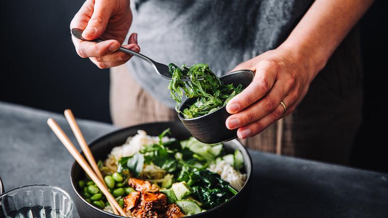 Close up a salad with chopped salmon, spinach, brussel sprouts, wakame, and chia seeds in a bowl.