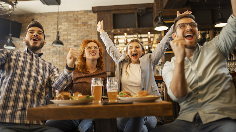 Group of friends at a bar watching a game and cheering.