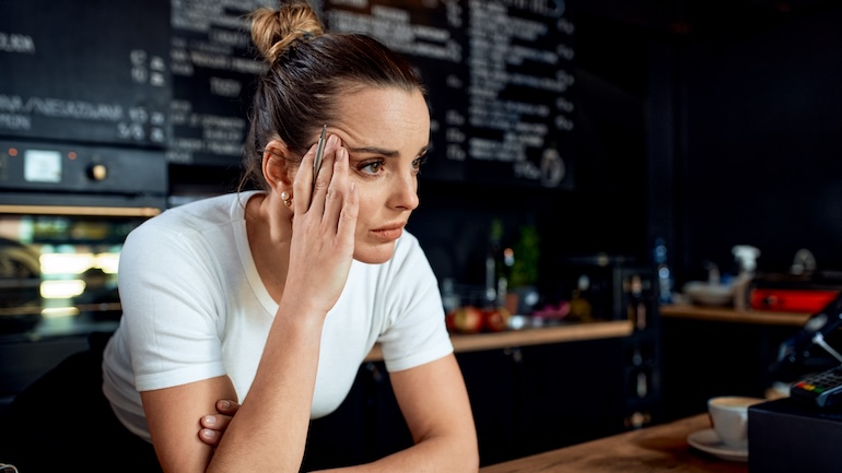 Woman who works at a restaurant is resting her hand on her face.