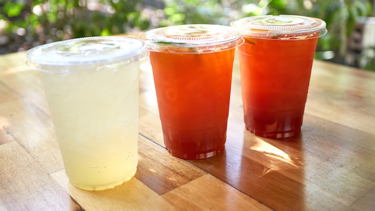 Iced lemon tea and honey lemon soda in plastic cups with lids placed on wooden tables.
