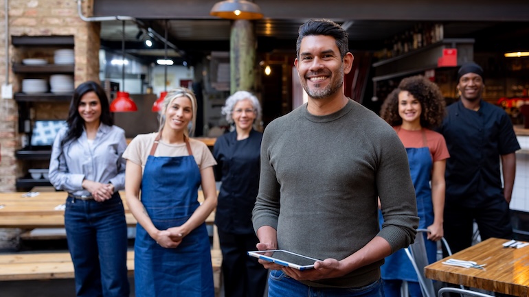 6 restaurant staff members smiling in front of a restaurant.